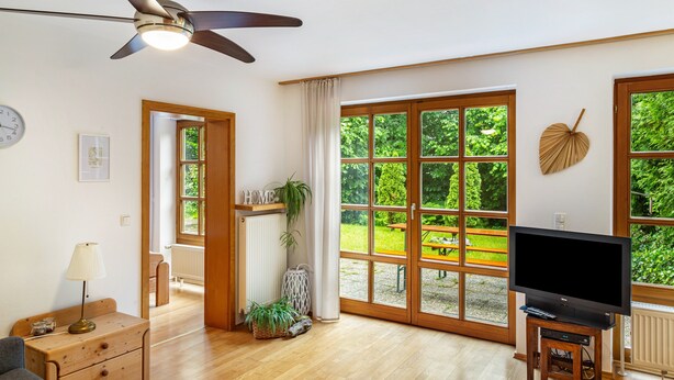 Ein geräumiges Zimmer mit Deckenventilator, großen Fenstern, einem Fernseher und Holzboden.