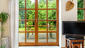 Ein Zimmer mit einer großen Schiebeglasdoor zum Garten, einem Flachbildfernseher auf einem Holzständer und einer Wanddekoration in Form eines Blattes.
