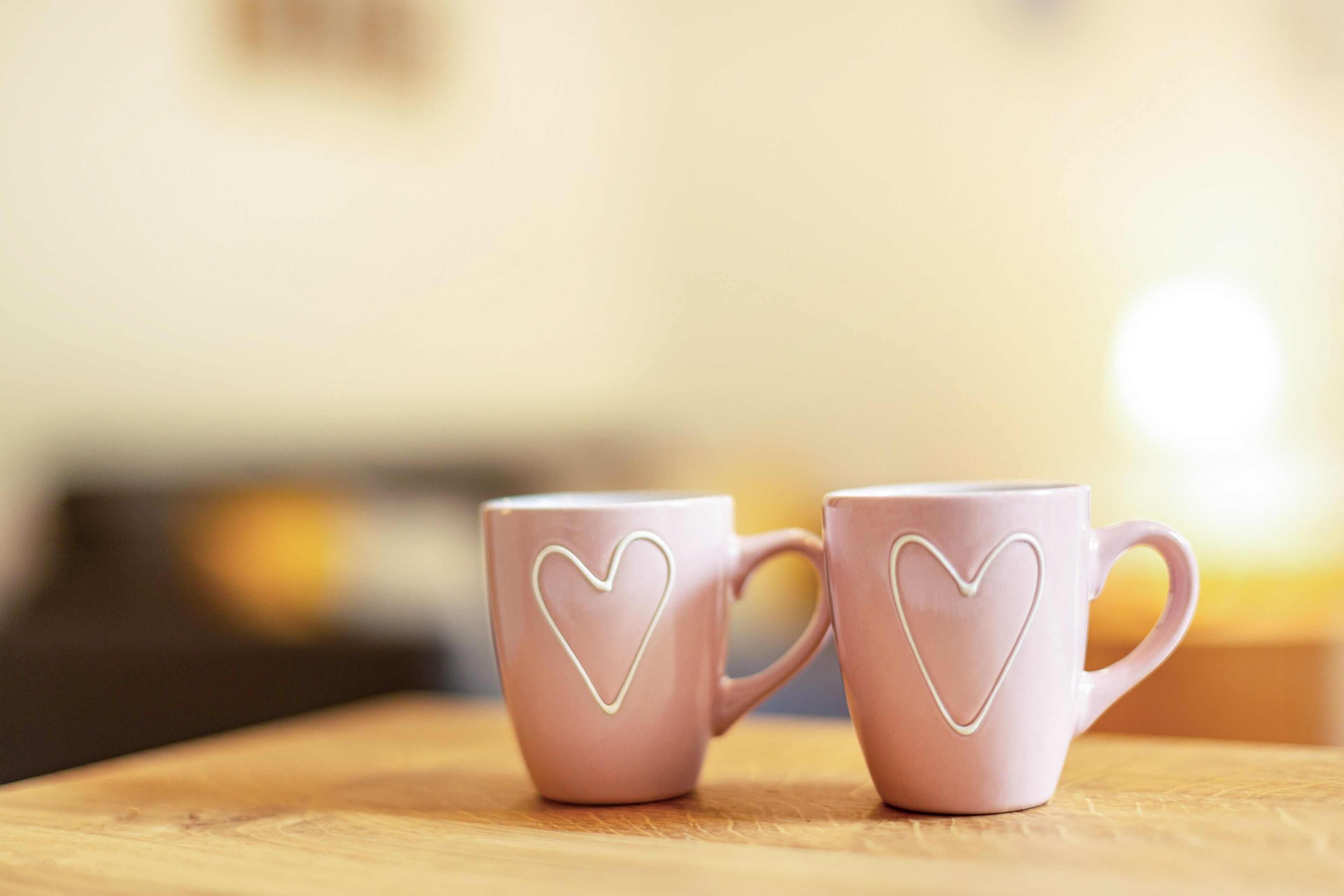 Deux tasses roses ornées de motifs en forme de cœur, posées sur une surface en bois.