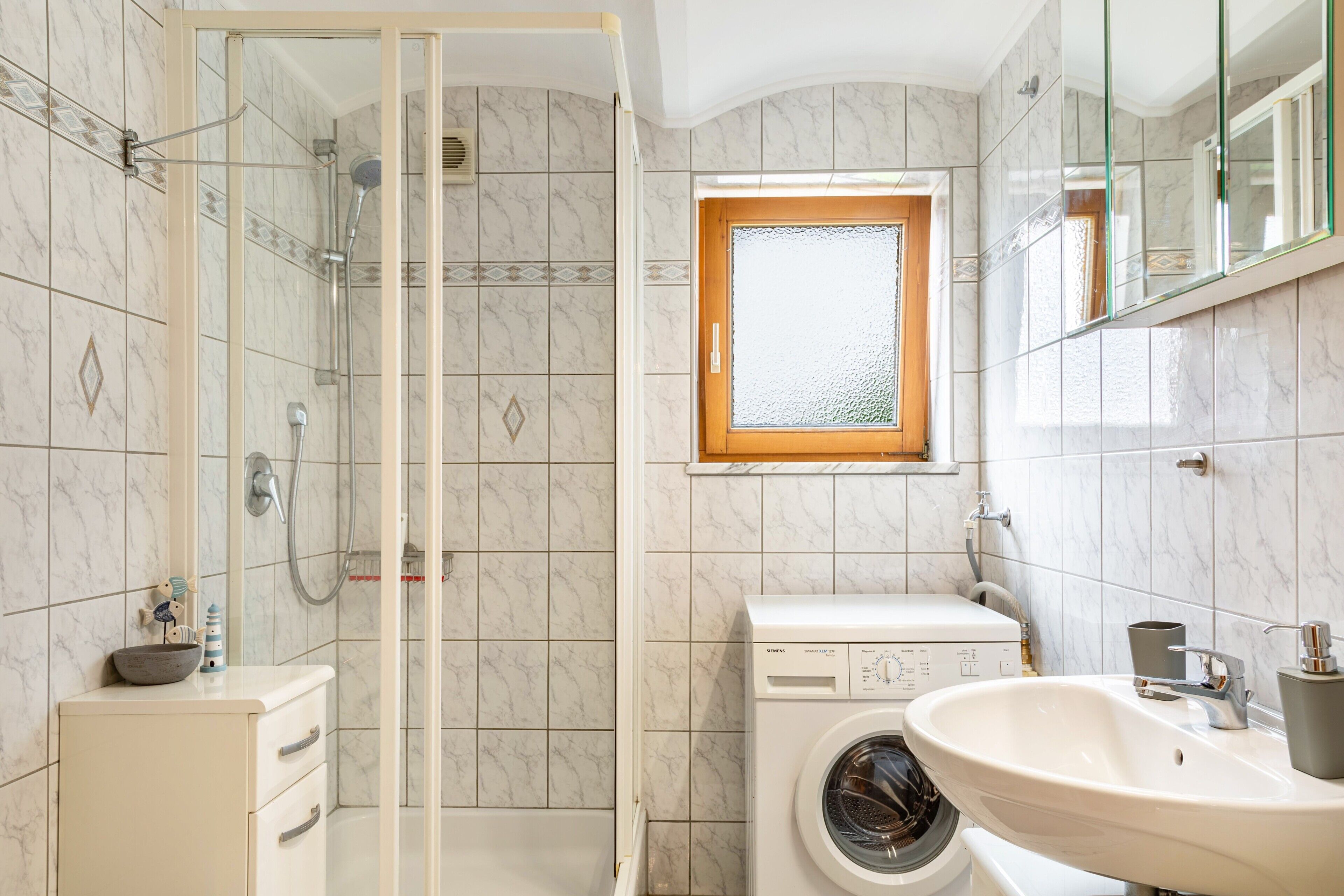Een badkamer met een douchecabine, een wasmachine, een wastafel en een raam.