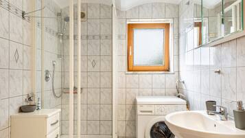 Een badkamer met een douchecabine, een wasmachine, een wastafel en een raam.