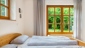 Ein Schlafzimmer mit Holz-Kopfteil, einem großen Fenster mit Vorhängen und einem Bett mit gestreifter Bettwäsche.