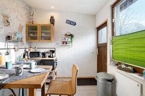 A compact kitchen with wooden cabinets, a microwave, and a dining area with a wicker chair. - Apartment "Wildwest Lounge" with Pool, Terrace & Wi-Fi (Eppingen)