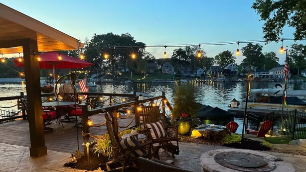 An outdoor patio with wicker furniture, string lights, and a view of a marina. - HEAVENLY Portage Lakes water front 4-bedroom cottage with HOTTUB, dog friendly! (Akron)