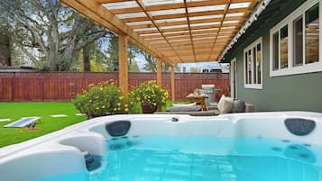 A backyard with a hot tub, wooden pergola, and a barbecue area.