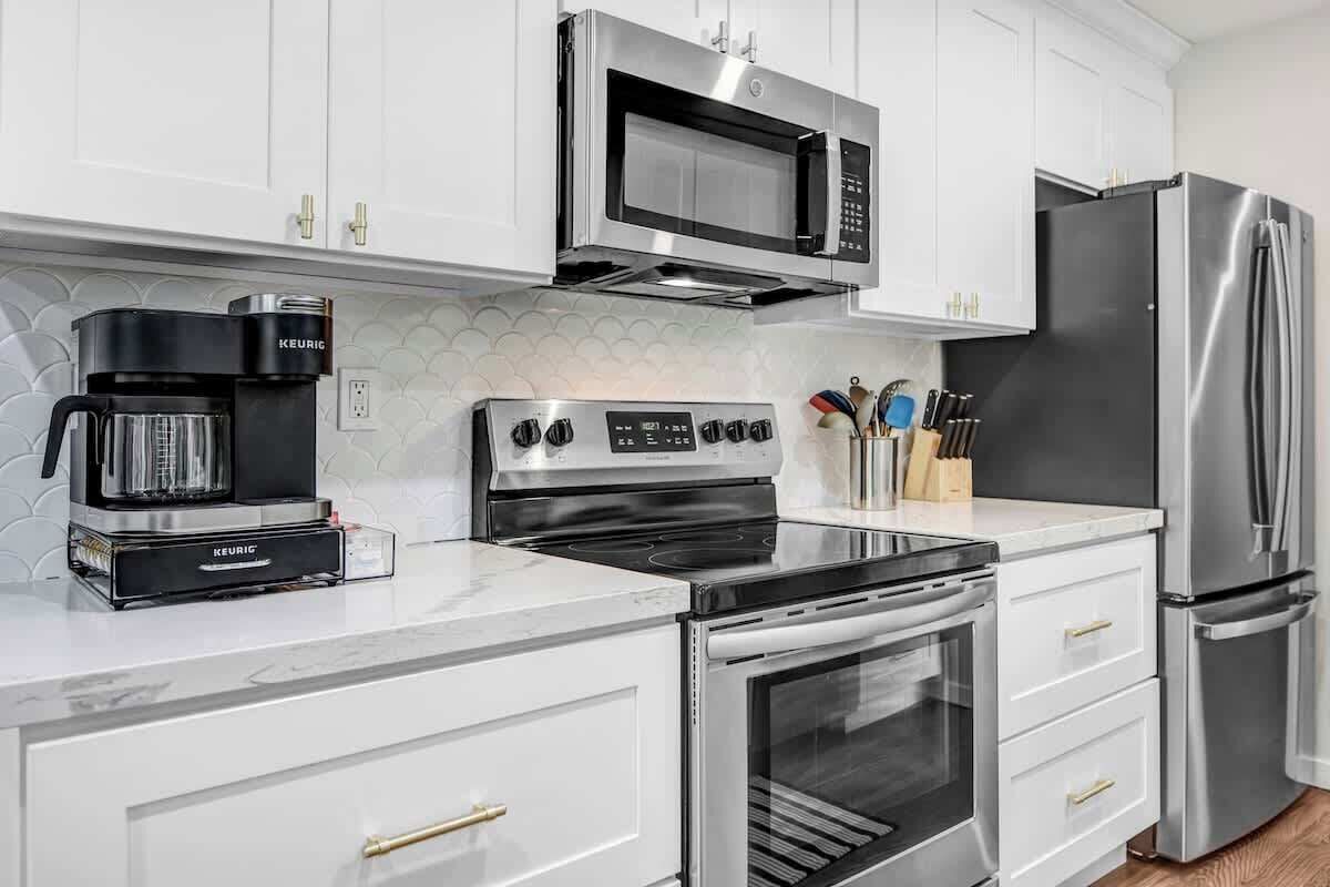 Una cocina moderna con electrodomésticos de acero inoxidable, armarios blancos y encimera de mármol.