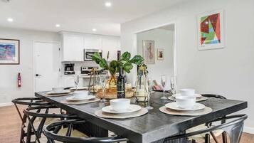 A modern dining area with a long table set for four, surrounded by black chairs.