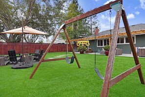A backyard with a wooden swing set, a patio table, and chairs. - Wine Country Backyard Escape (Santa Rosa)