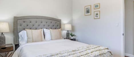 A bedroom with a bed, two bedside tables with lamps, a nightstand, and a door.