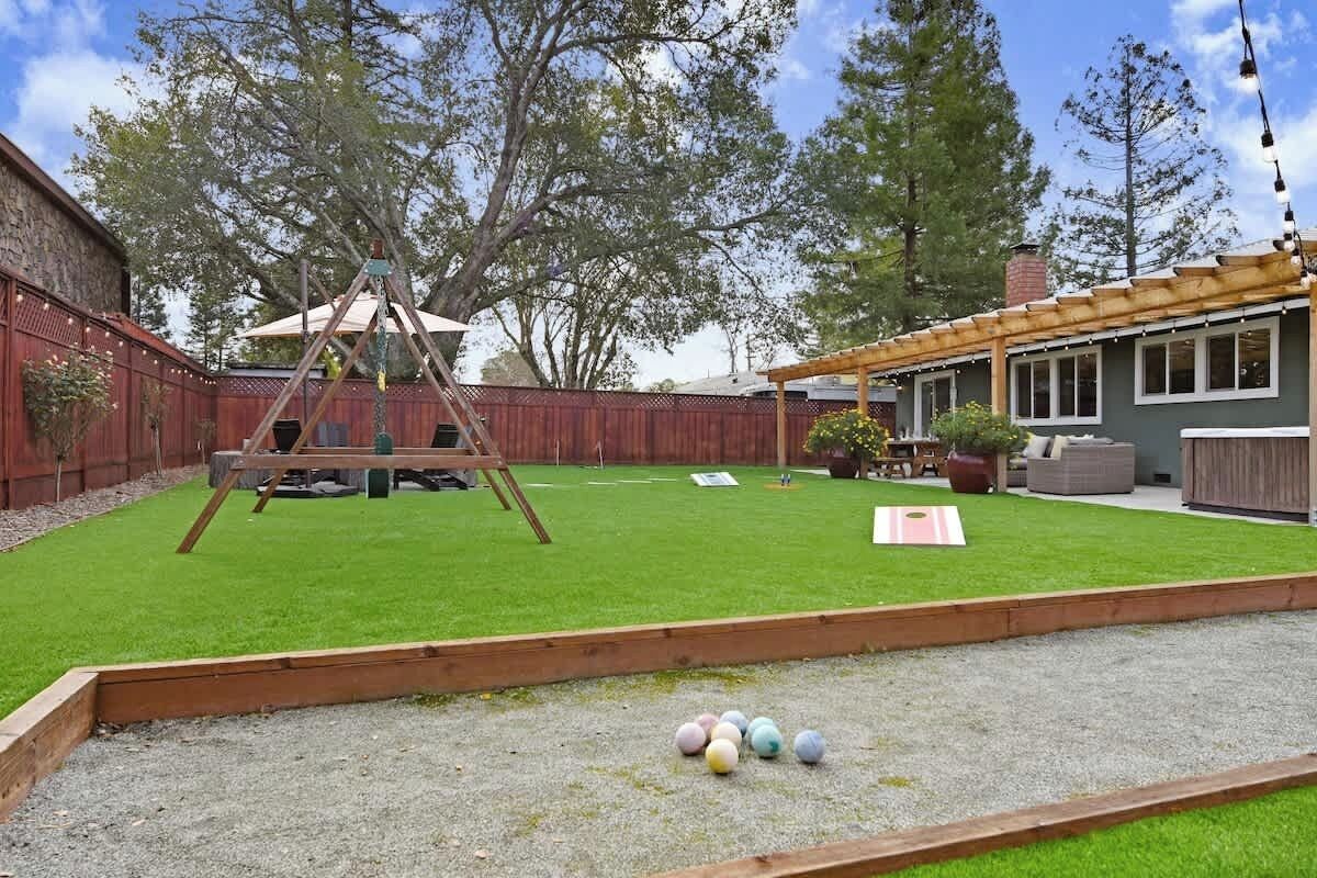 Ein Garten mit Schaukel, einer Pergola und einem Rasen mit bunten Bällen.