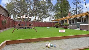 Ein Garten mit Schaukel, einer Pergola und einem Rasen mit bunten Bällen.