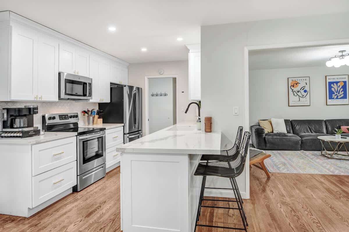 A modern kitchen with white cabinetry, stainless steel appliances, and a central island with bar stools.