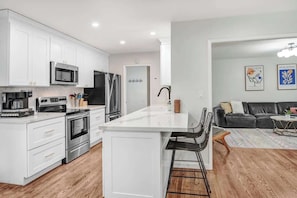 A modern kitchen with white cabinetry, stainless steel appliances, and a central island with bar stools. - Wine Country Backyard Escape (Santa Rosa)