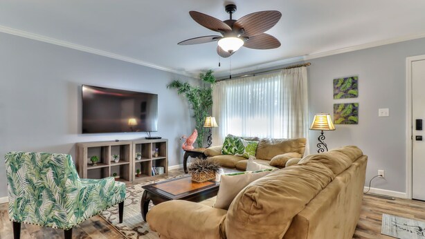 A living room with a flat-screen TV, a ceiling fan, a sofa, a coffee table, and a bookshelf. - Beautiful 4 bedroom 2 full bathroom close to everything! (Champaign)