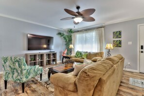 Ein Wohnzimmer mit Flachbildfernseher, Deckenventilator, Sofa, Couchtisch und Bücherregal.