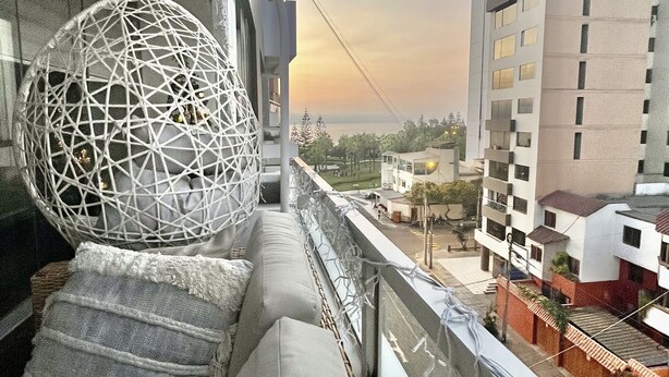 A balcony with a spherical hanging chair, a staircase, and a view of a cityscape with buildings. - Ideal location Ocean View Miraflores Condo (Miraflores)