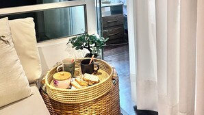 A modern living room with a large window, a wicker basket with bread and a teapot, a small plant, and a white sofa. - Ideal location Ocean View Miraflores Condo (Miraflores)