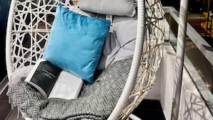 A hanging chair with cushions and a book, positioned near a window with a view of the city at night. - Ideal location Ocean View Miraflores Condo (Miraflores)