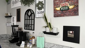 Une cuisine dotée de plans de travail en granit, d’une machine à café, d’une guirlande décorative suspendue et de divers éléments de décoration murale, dont une enseigne portant l’inscription « Gather Home ».