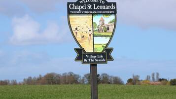 A welcome sign for Chapel St Leonard with a village life by the seaside illustration.