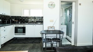 A modern kitchen with white cabinets, a black countertop, and a small dining table with chairs. - 57 Cherry Park (Skegness)