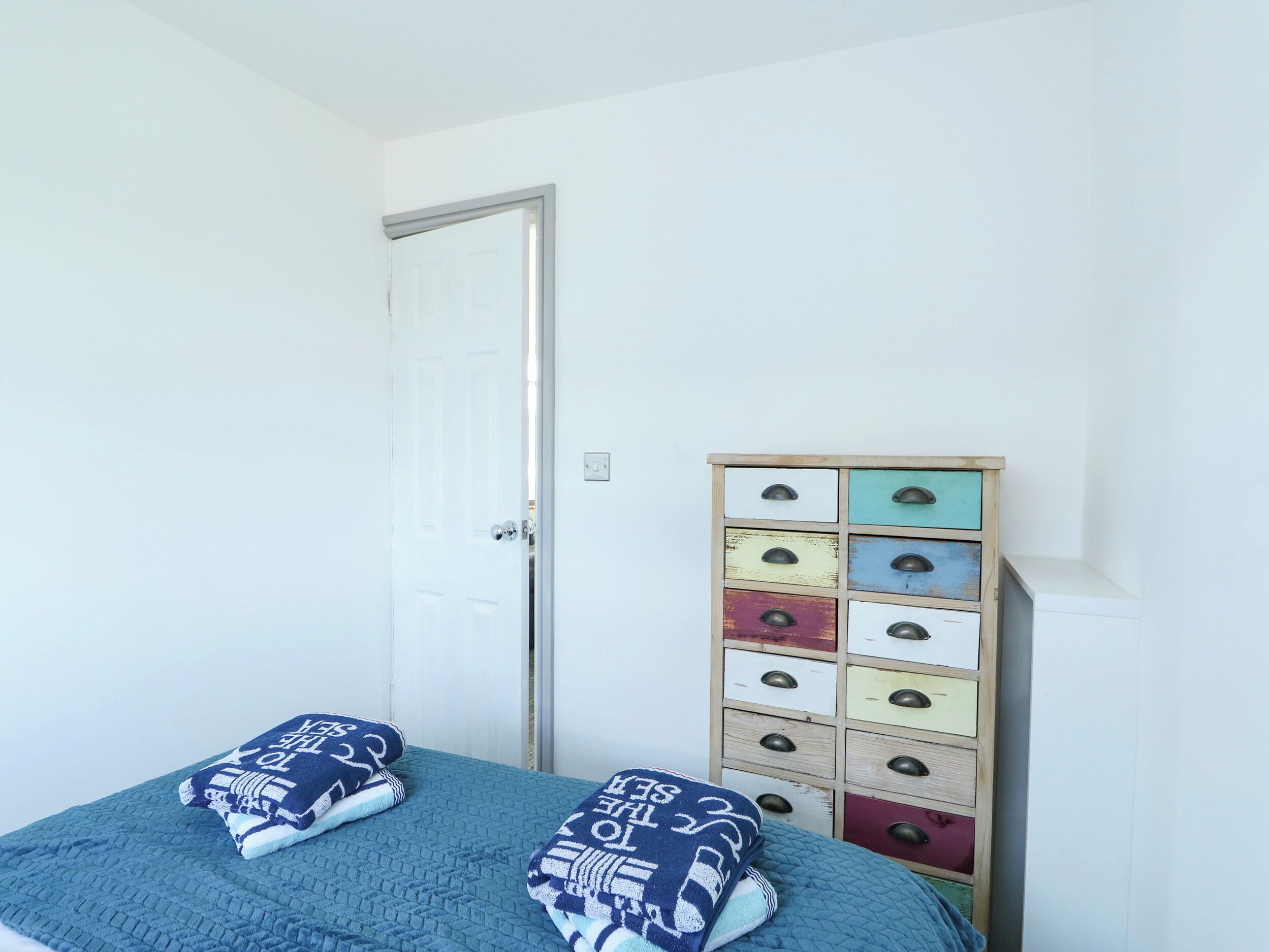A bedroom with a bed, two pillows, a wooden dresser with multiple drawers, and a white door.