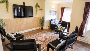 Un salon équipé d’un téléviseur à écran plat, de deux fauteuils noirs, d’un tapis rouge à motifs et d’un mur recouvert de panneaux en bois.