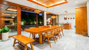 Un comedor moderno con una gran mesa de madera y sillas, una cocina con armarios de madera, y un ventanal que da a un espacio exterior.