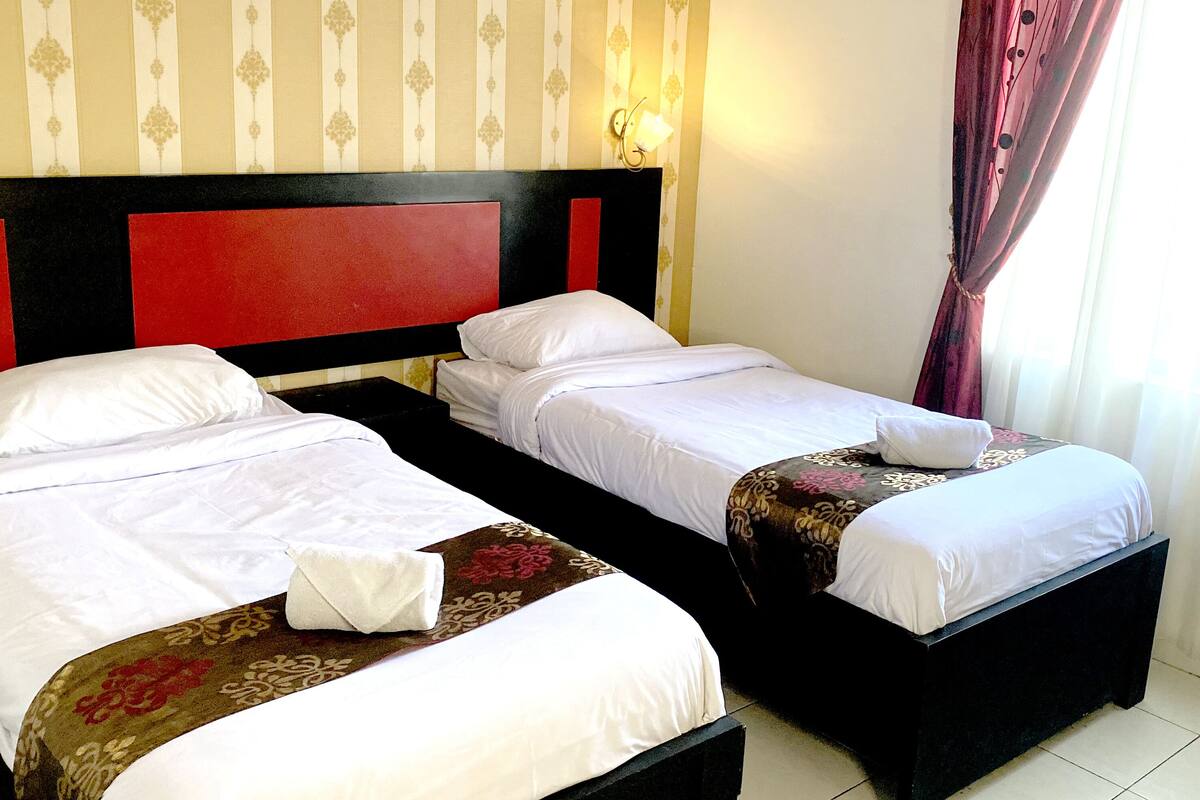 A hotel room with two beds, each with white linens and a red headboard.