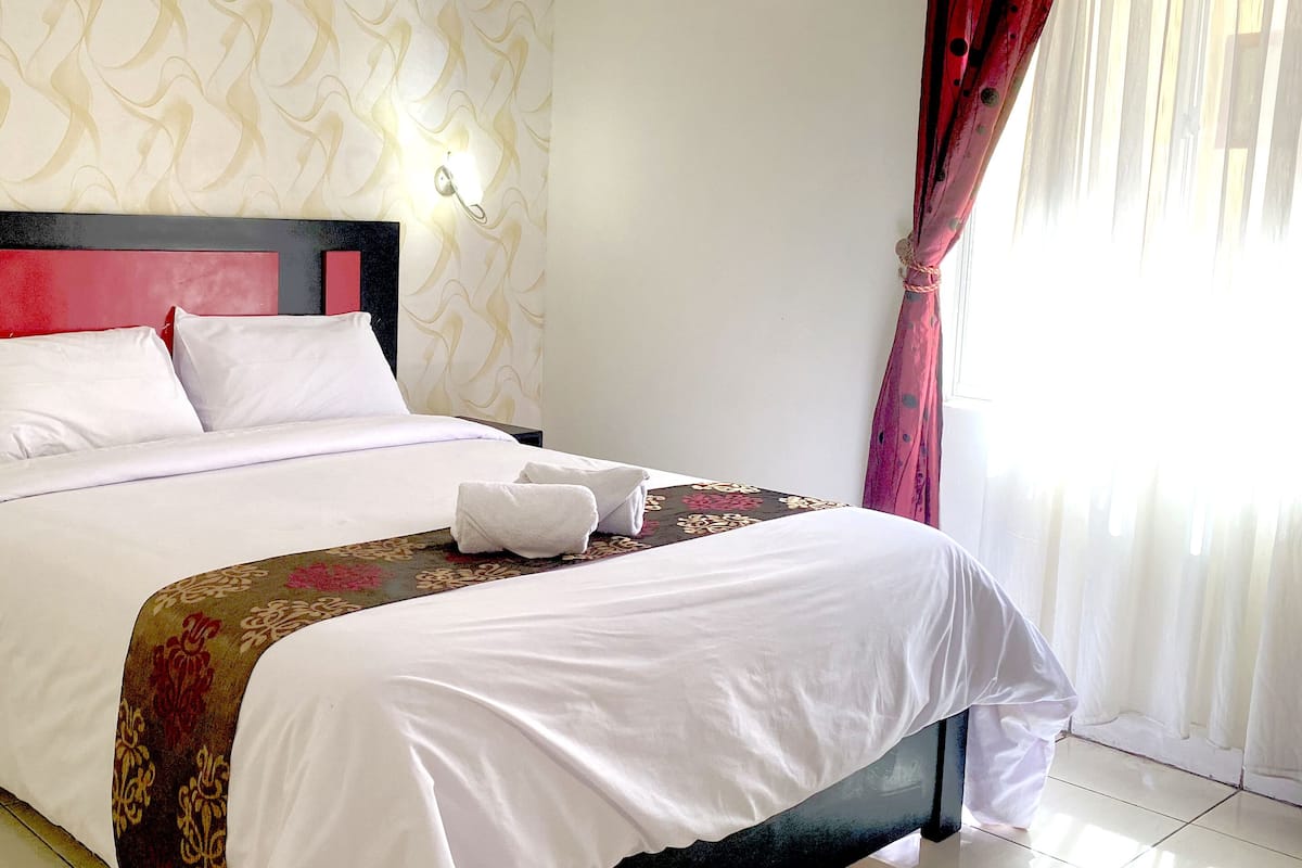 A hotel room with a bed, a bedside table with a phone, and a decorative headboard.