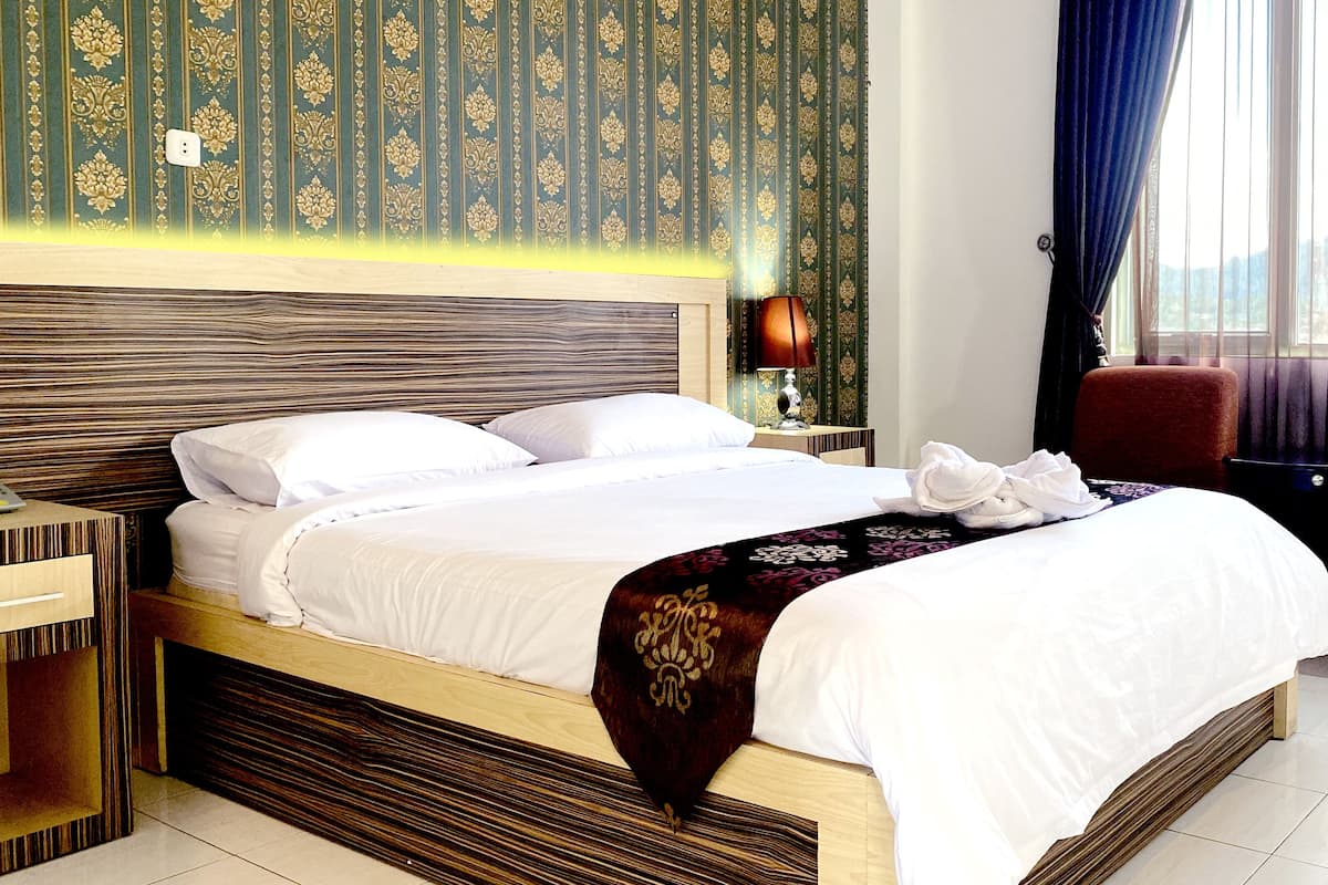 A hotel room with a large bed, a nightstand, a lamp, a chair, and a view of the outdoors.