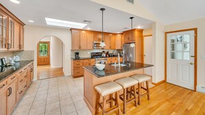 A spacious kitchen with wooden cabinets, a central island with stools, and a large window. -  Southampton Gem House with Beautiful Heated Pool (Southampton)