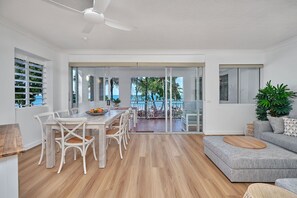 Ein modernes Wohnzimmer mit Essbereich, große Schiebeglastüren zu einem Balkon mit Meerblick und einem Deckenventilator.