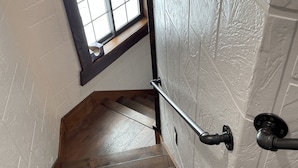 Un escalier en bois avec une rampe métallique, une fenêtre en haut et un mur blanc à texture.