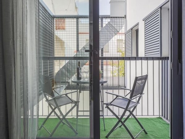 A balcony with a glass door, two chairs, a small table, and a bottle of wine.