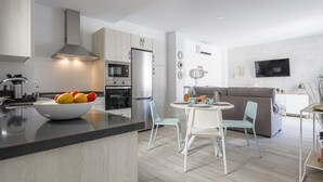 Une cuisine moderne dotée d’appareils électroménagers intégrés, un coin repas avec une table ronde et des chaises, et un salon avec un canapé et un téléviseur.
