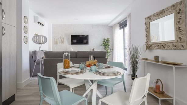 Un espace repas moderne avec une table ronde, des chaises bleu clair et blanches, et un canapé gris en arrière-plan.