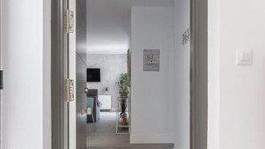 Un couloir au plancher de bois menant à une cuisine équipée d’un meuble blanc et agrémentée d’une plante.