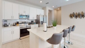 Una cocina moderna con armarios blancos, electrodomésticos de acero inoxidable, una isla central con taburetes altos y un elemento decorativo en la pared.