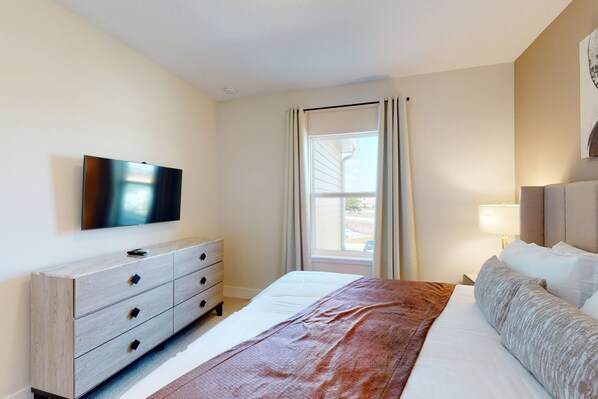 A hotel room with a bed, a TV mounted on the wall, a dresser, and a window with curtains.
