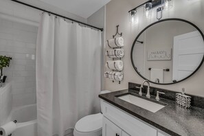 Een badkamer met een witte badkuip, toilet, wastafel met een marmeren aanrechtblad, een ronde spiegel en handdoeken aan haken.