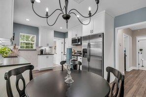 Een moderne keuken met witte kasten, een roestvrijstalen koelkast en een eethoek met een zwarte tafel en stoelen.