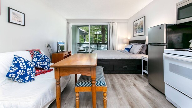 A compact living space with a sofa, a wooden dining table, a kitchenette, and a sliding glass door leading to an outdoor area.