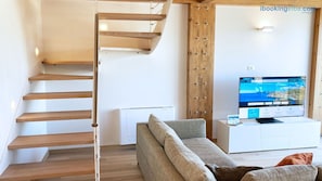 Un soggiorno moderno con una scala in legno, una televisione a schermo piatto e un divano.
