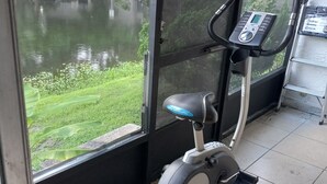 Uma bicicleta de exercício num quarto com uma janela ampla com vista para a água e vegetação.