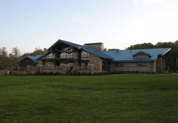 A large, modern house with a stone facade, a prominent gable roof, and a spacious front yard.