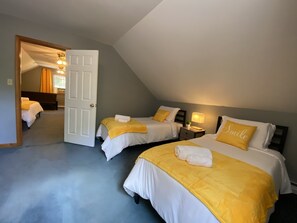 A hotel room with two beds, each with a yellow bedspread and white pillows, including one with the word "Smile". There is a nightstand with a lamp between the beds, and a door leading to another room.