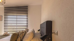 A bedroom with a bed, pillows, a bedside lamp, a small plant, and a window with blinds. - Penthouse with Terrace San Julian Cordoba ⭐⭐⭐⭐ (CORDOBA)