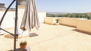 A rooftop terrace with a retractable awning, a potted plant, and a view of a distant building. - Penthouse with Terrace San Julian Cordoba ⭐⭐⭐⭐ (CORDOBA)