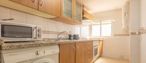 Una cocina con microondas, lavadora y cafetera sobre la encimera.